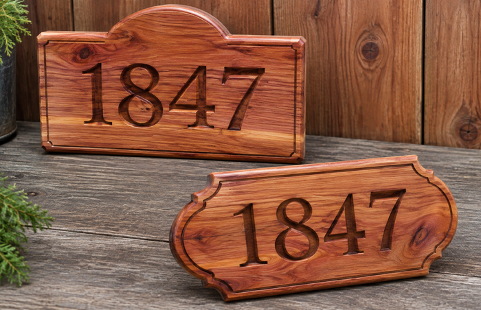 Two custom wooden house numbers displaying '1847' carved into the wood, shown on a rustic wooden surface with a wooden plank wall background.